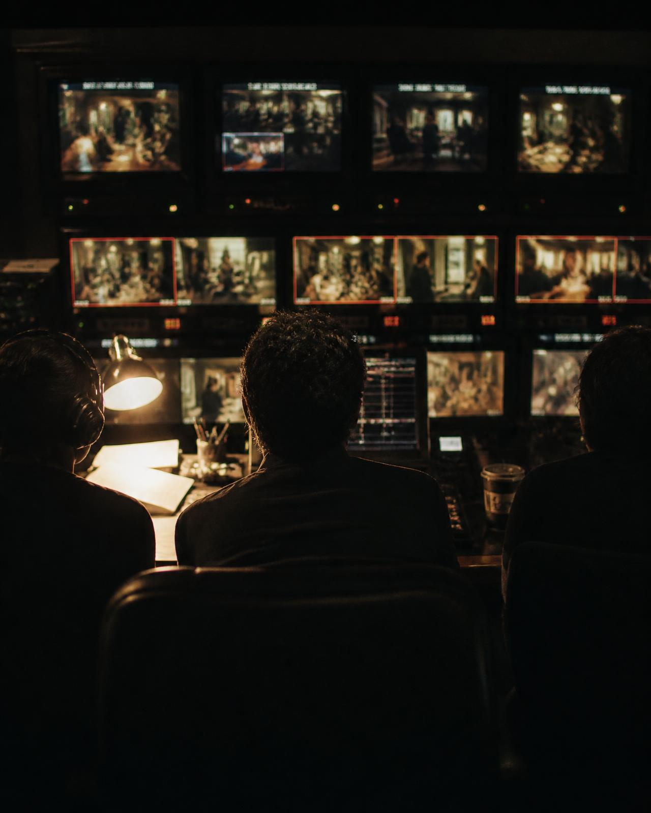 Production team working at a wall of monitors in a dimly lit television gallery